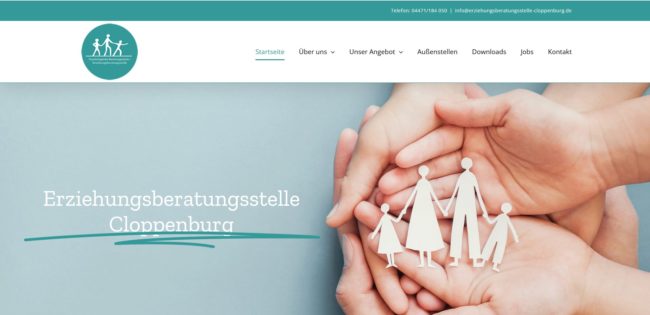 Mehrere Hände halten Papierfiguren einer Familie, darüber steht der Text "Familienberatung Cloppenburg" auf einer Webseite mit türkisem Design und Navigationsmenü oben.